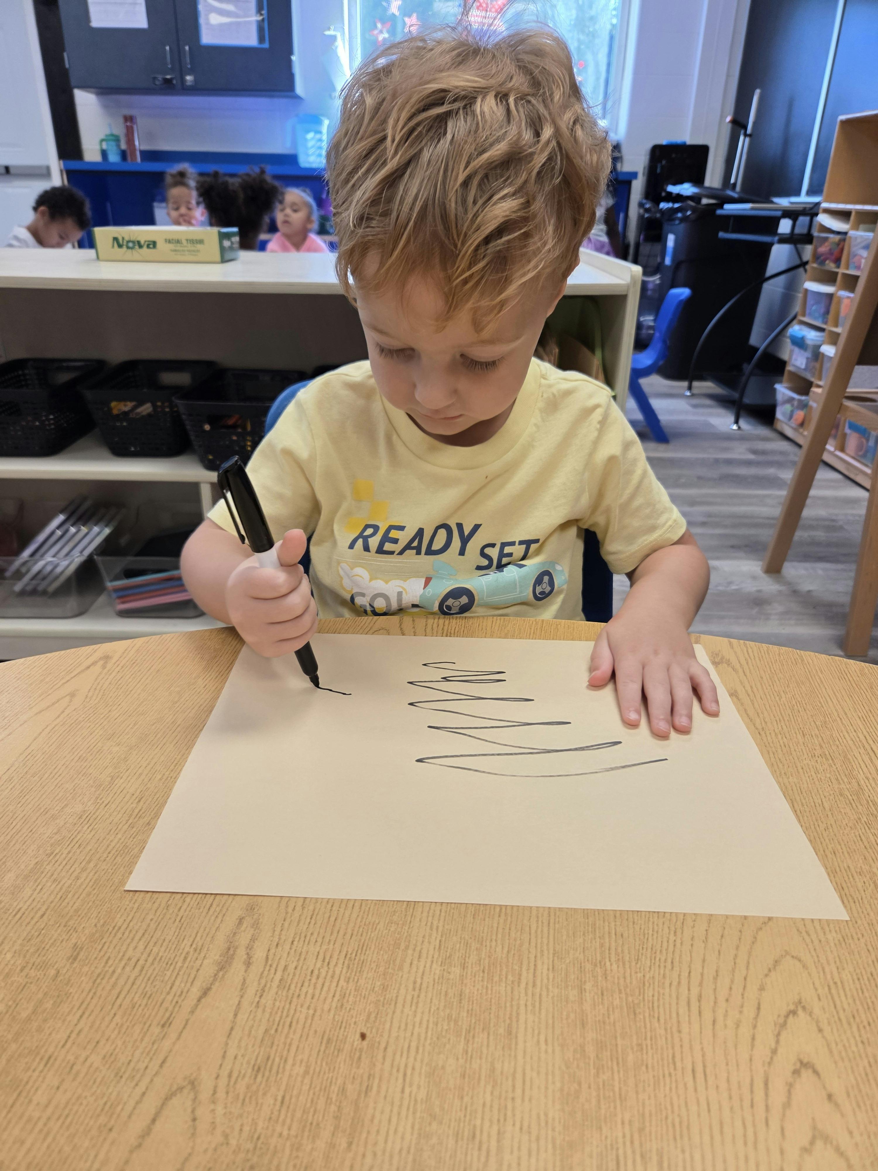 Child drawing on paper with a marker in a classroom