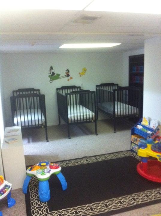 Multiple cribs in a room with a rug and toys