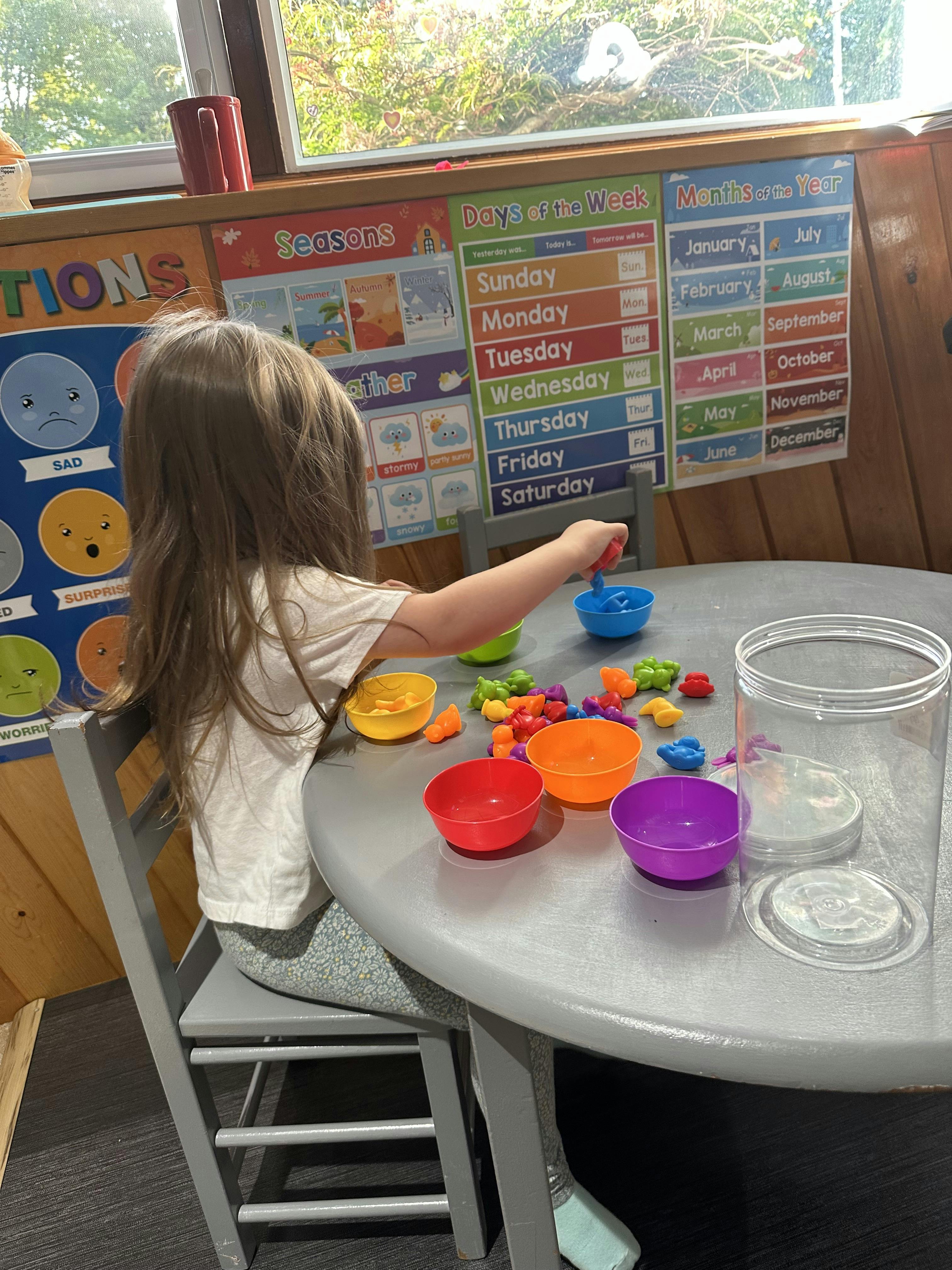 Child playing with colorful bowls and small objects at a table