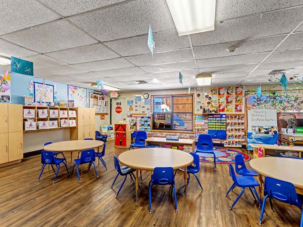 Classroom with small tables and chairs, cubbies, and colorful displays