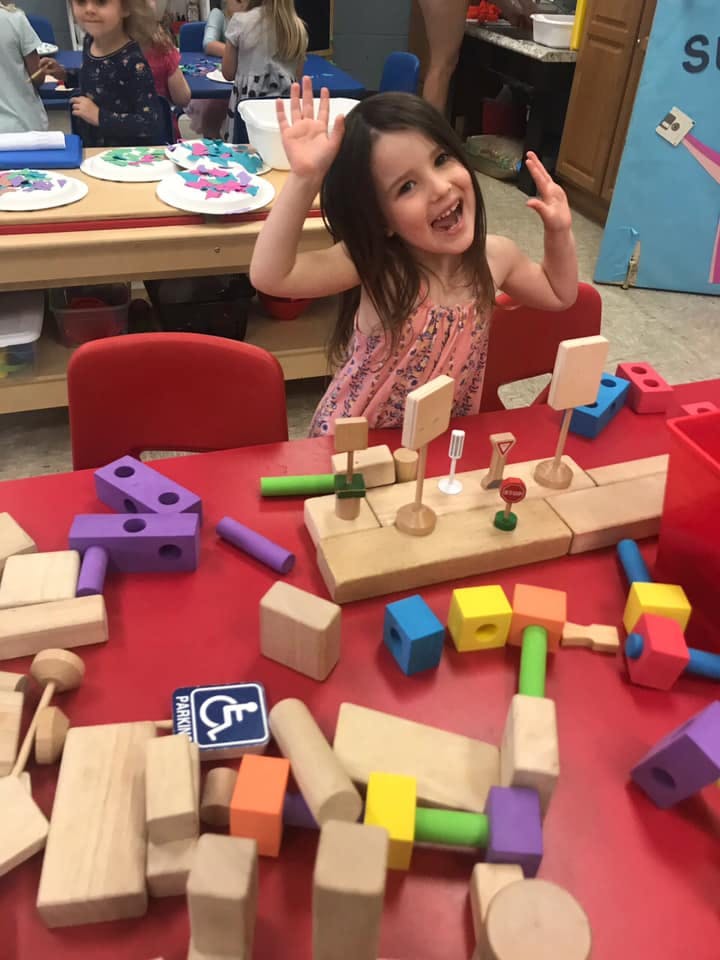 Child with hands raised sitting at a table with blocks