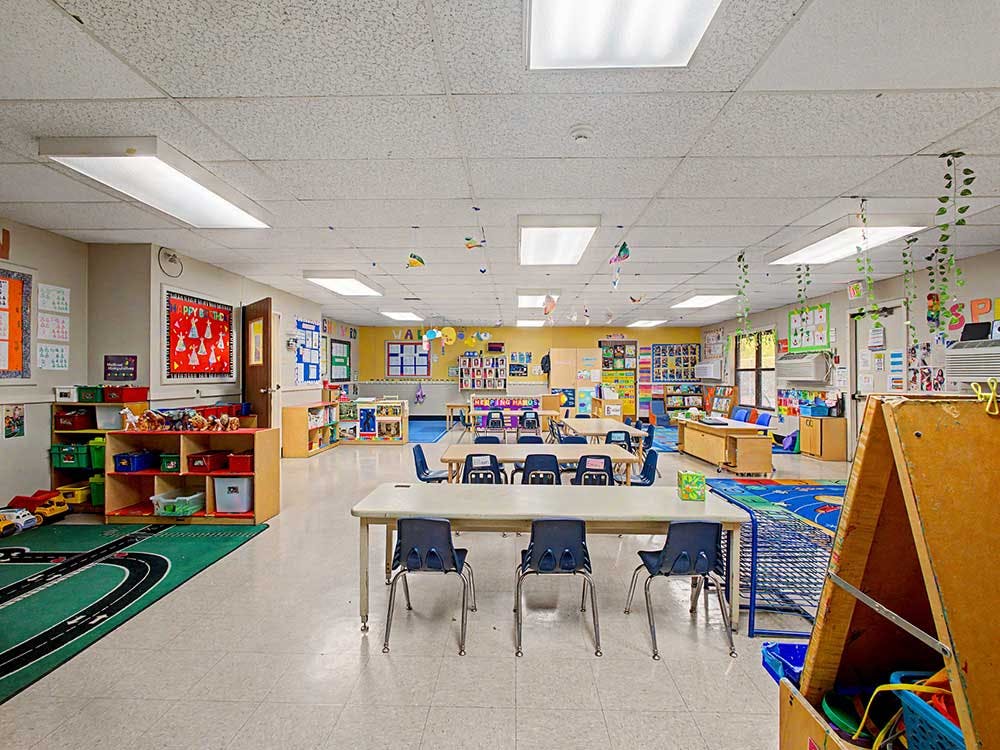 Empty classroom with small tables and chairs, shelves with toys and books