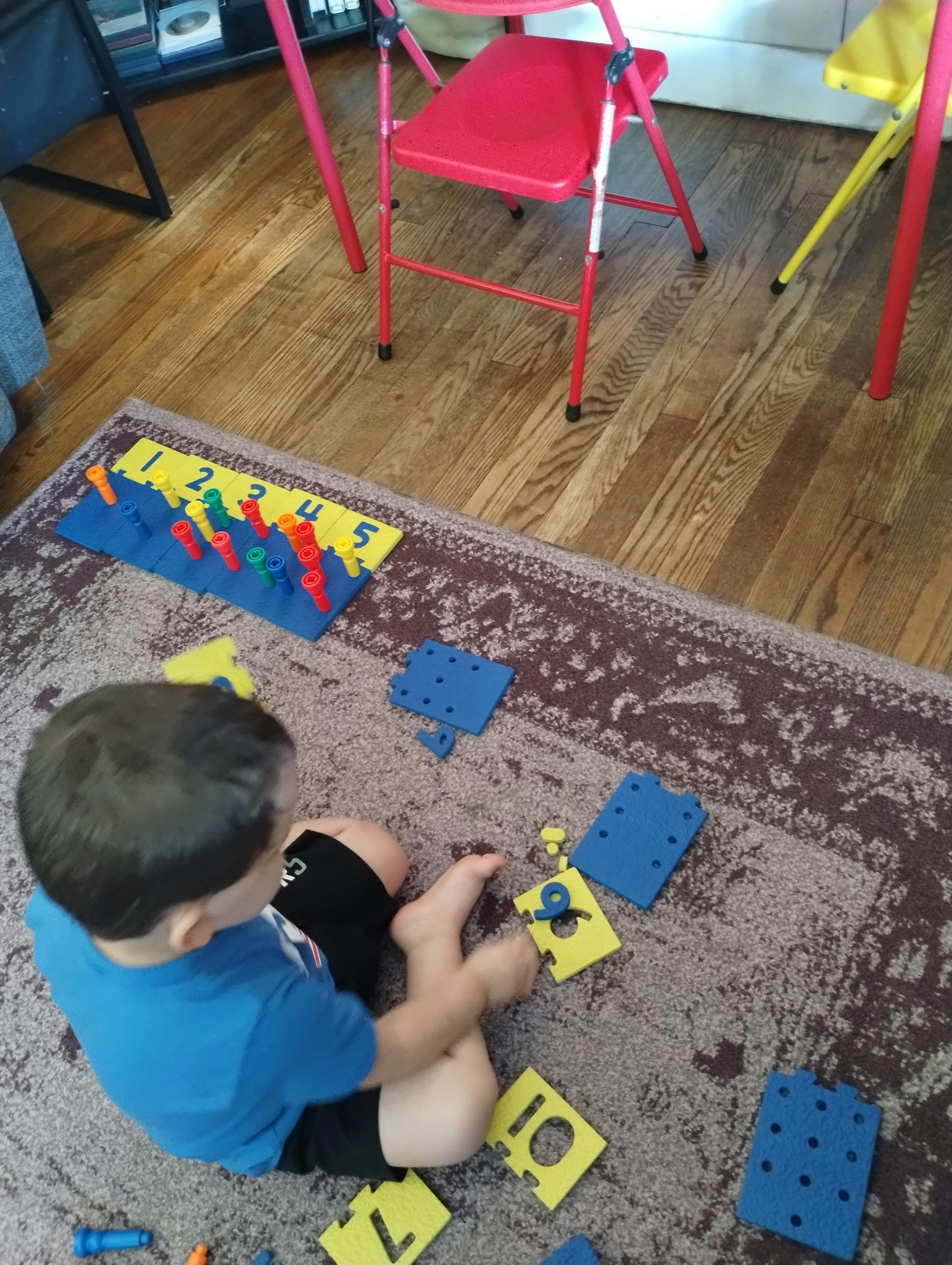 Child sitting on a rug playing with a number peg board and puzzle pieces