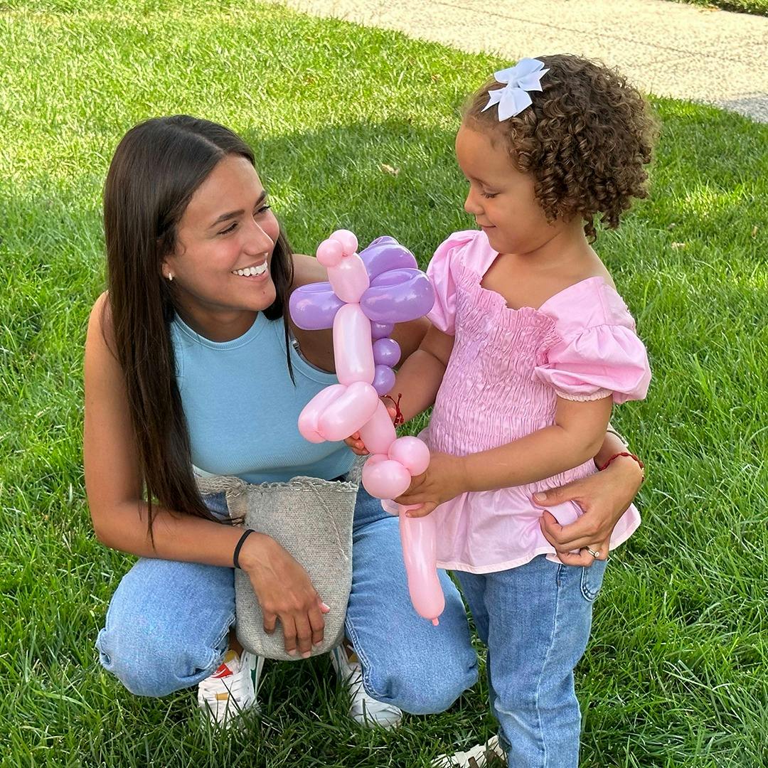 Person crouching with a child holding a balloon animal
