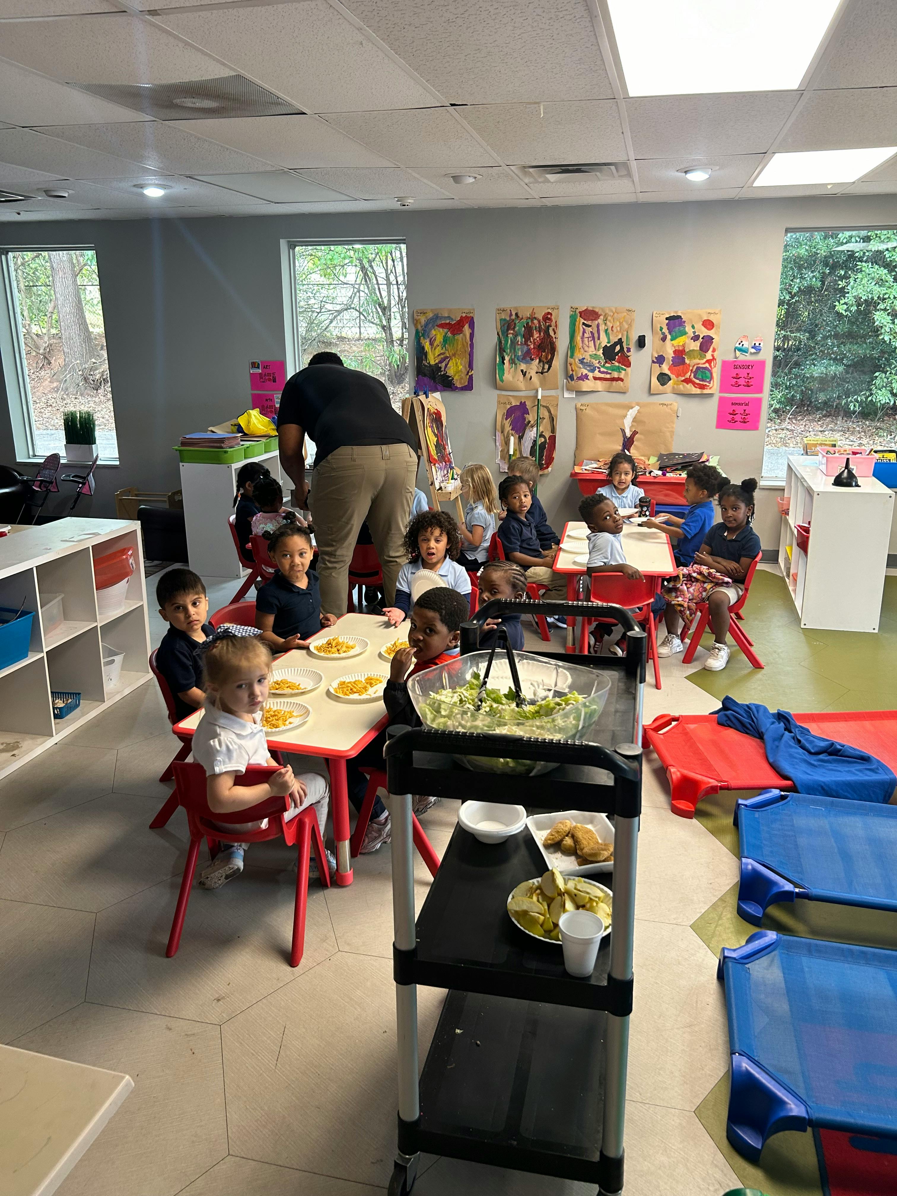 Person serving food to children seated at tables in a classroom