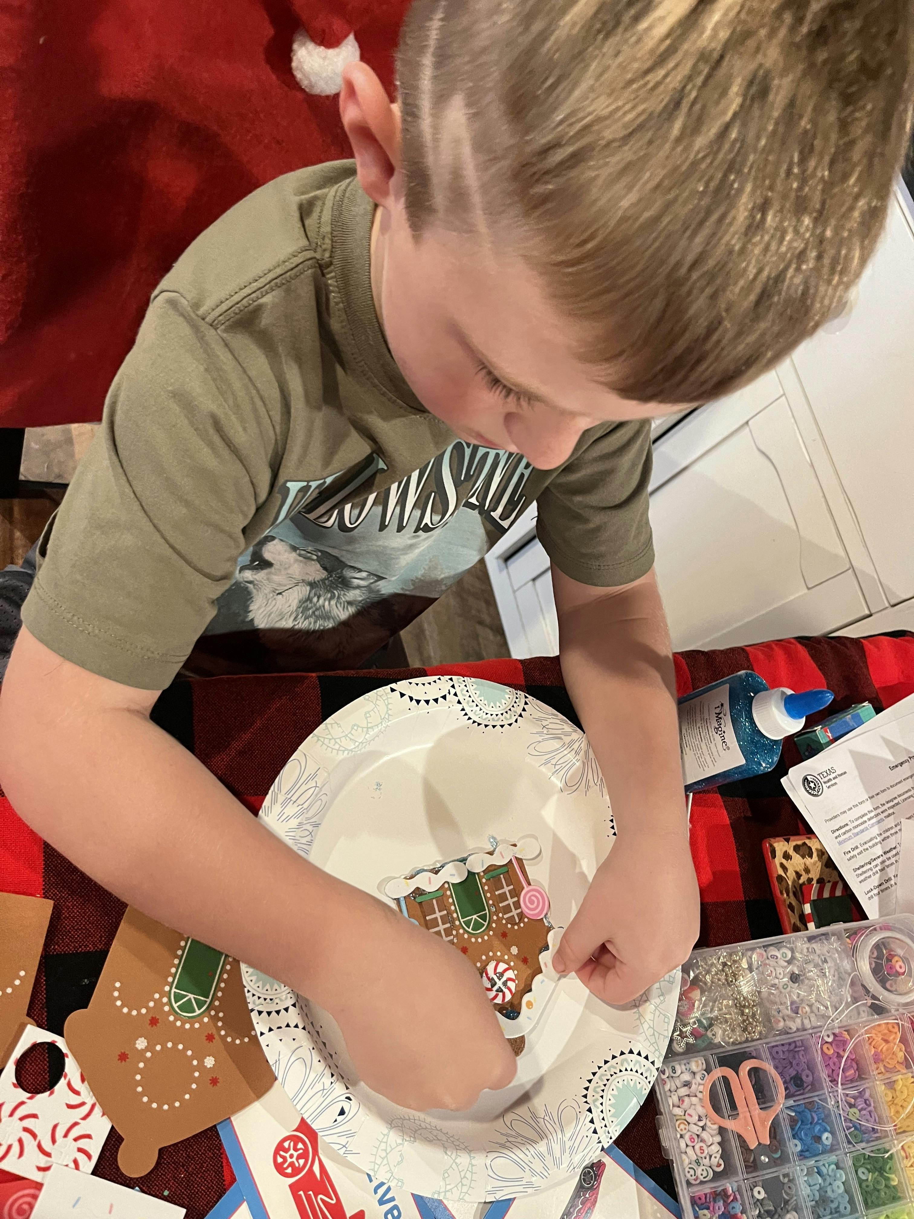 Child decorating a gingerbread house craft on a paper plate