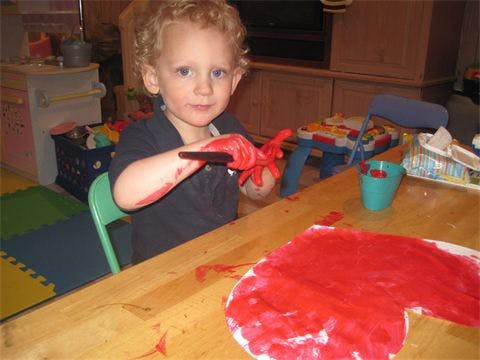 Child with red paint on hands and paper at a table
