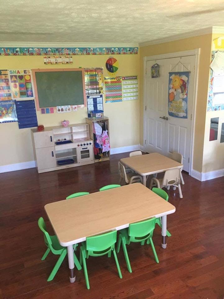 Classroom with small tables and chairs, chalkboard, and play kitchen
