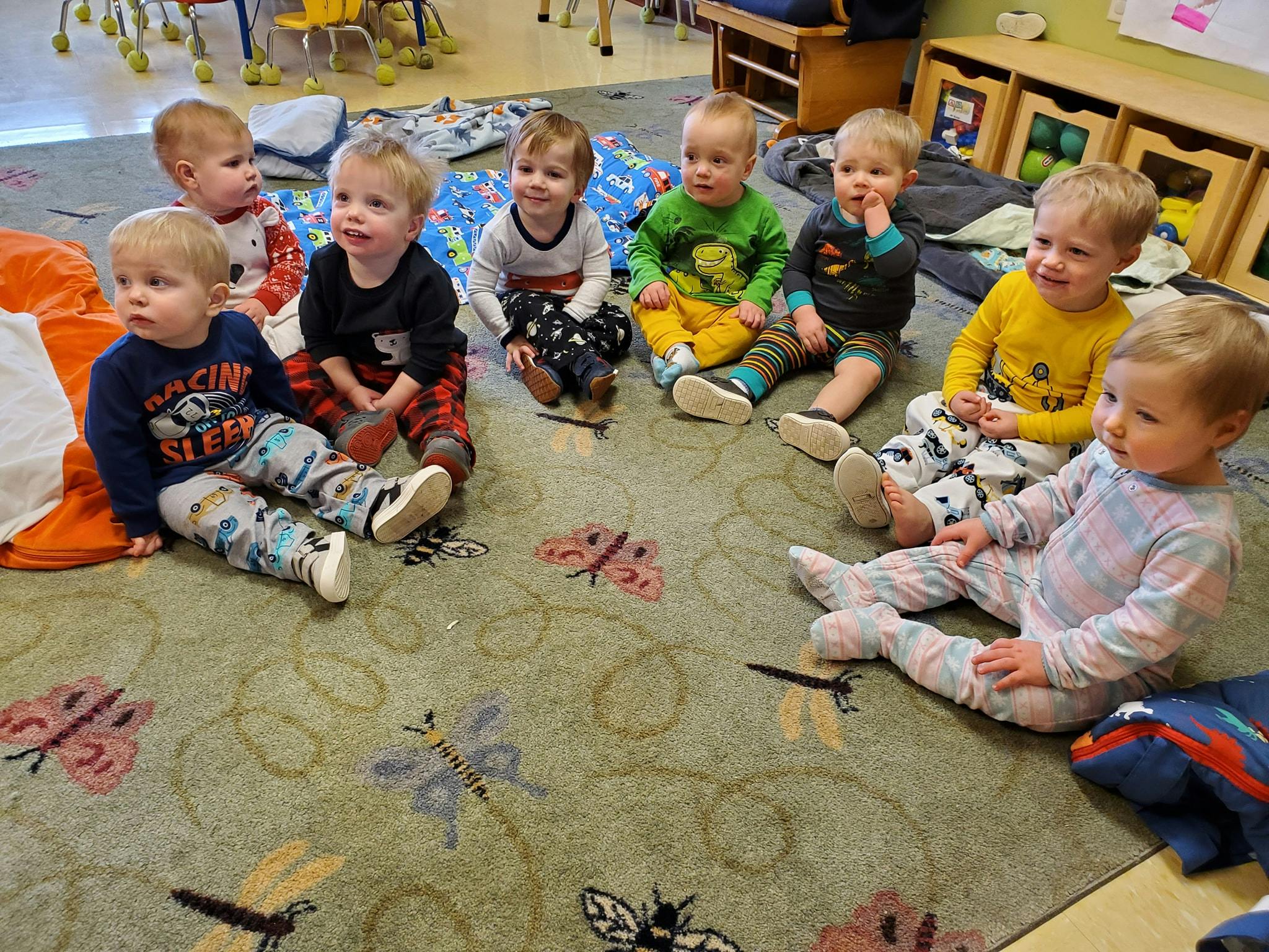Seven children sitting on a rug in a classroom