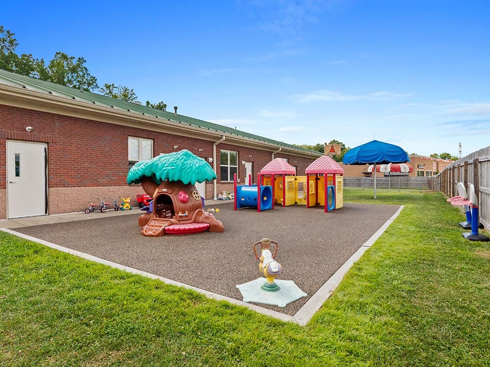 Outdoor playground with a treehouse structure, colorful playhouses, and a seesaw