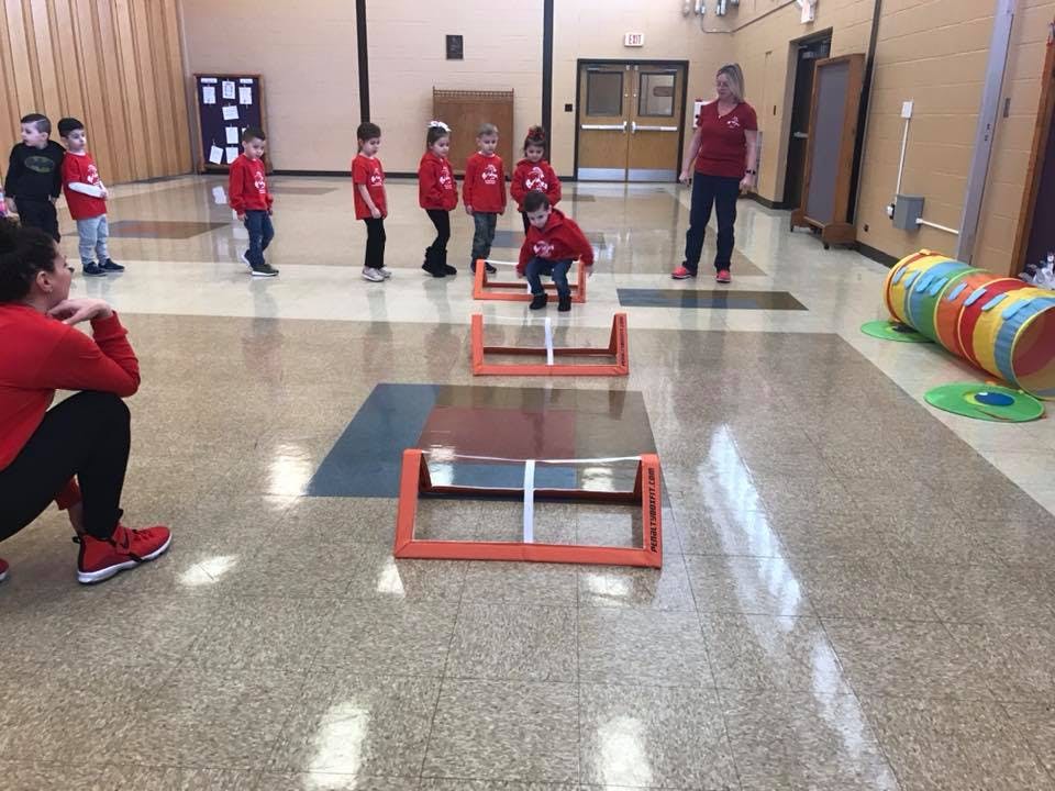 Children and adults in a gym with hurdles and a tunnel