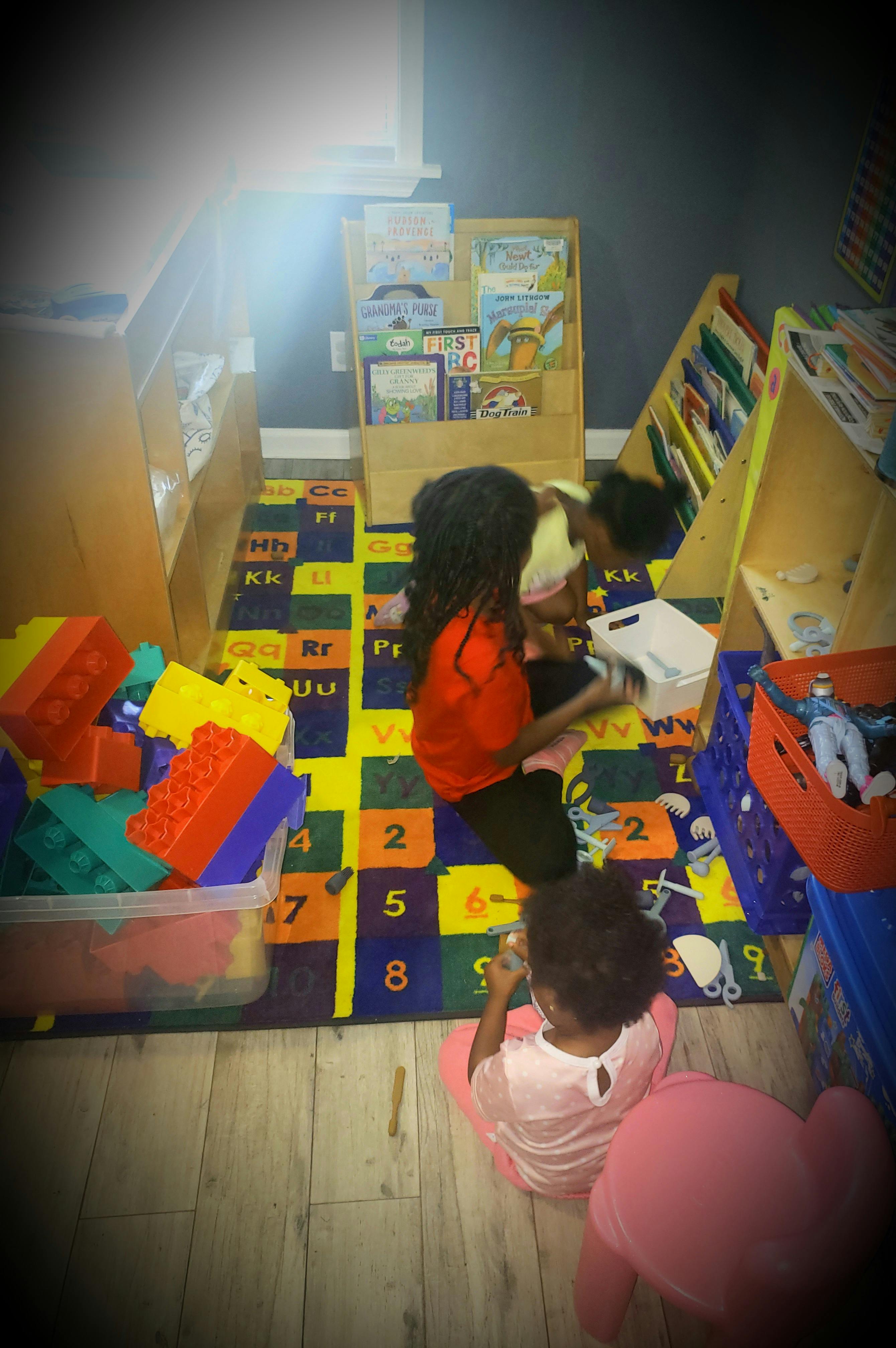 Three children playing on a colorful alphabet and number rug in a classroom