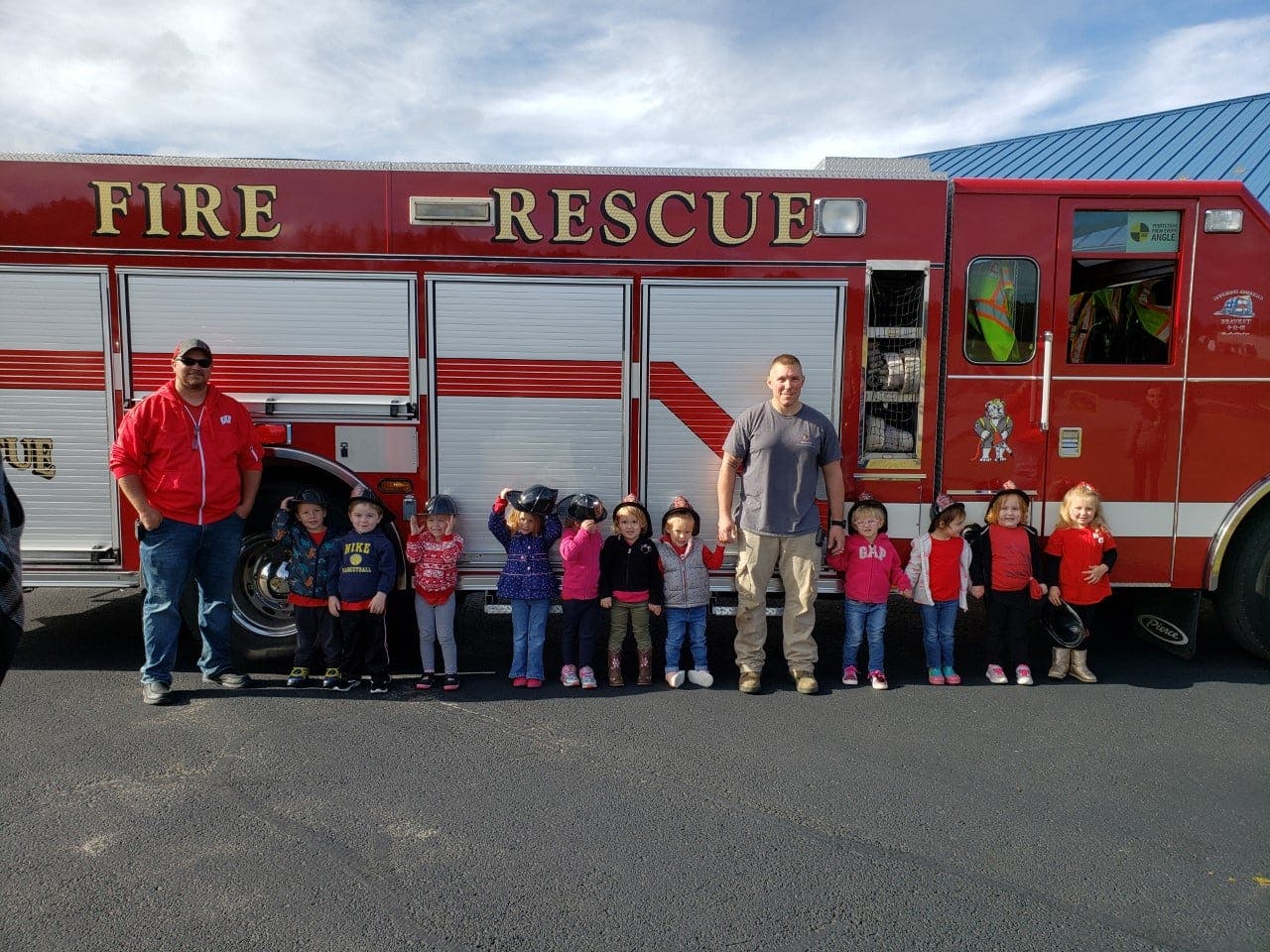 Two people and multiple children standing in front of a fire truck