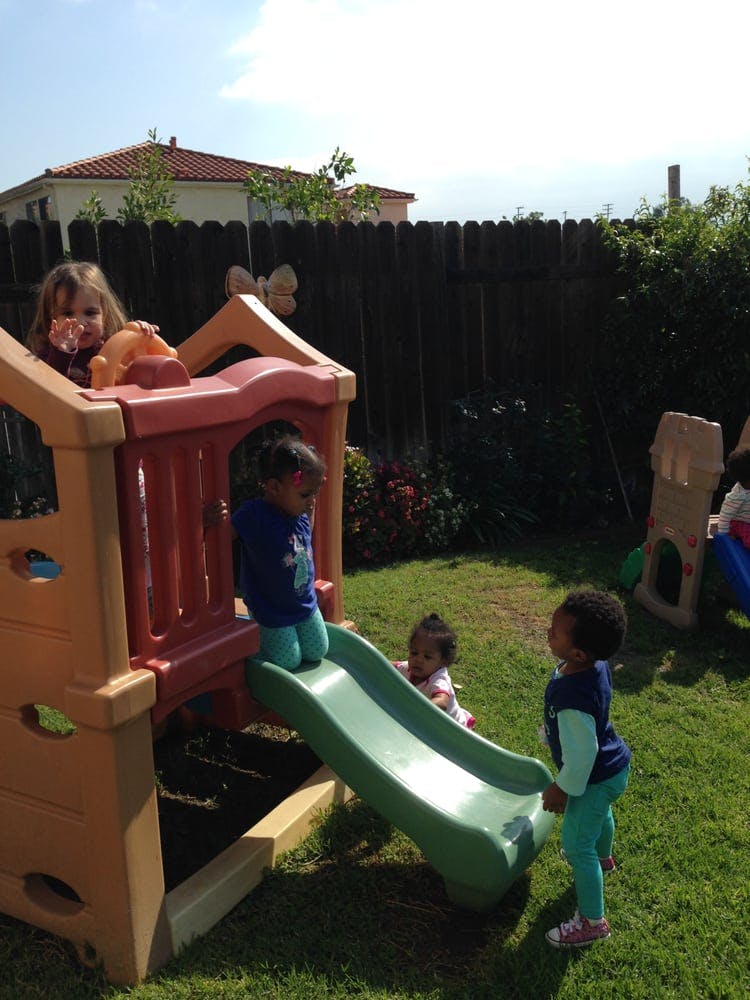 Children playing on a slide and play structure in a grassy yard