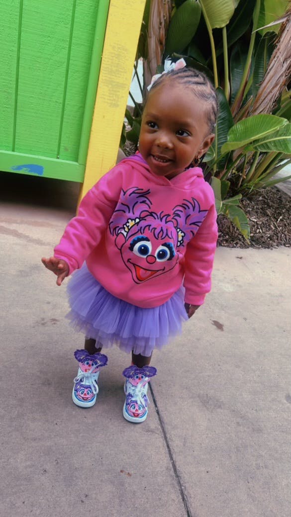 Child wearing an Abby Cadabby sweatshirt, purple tutu, and matching sneakers