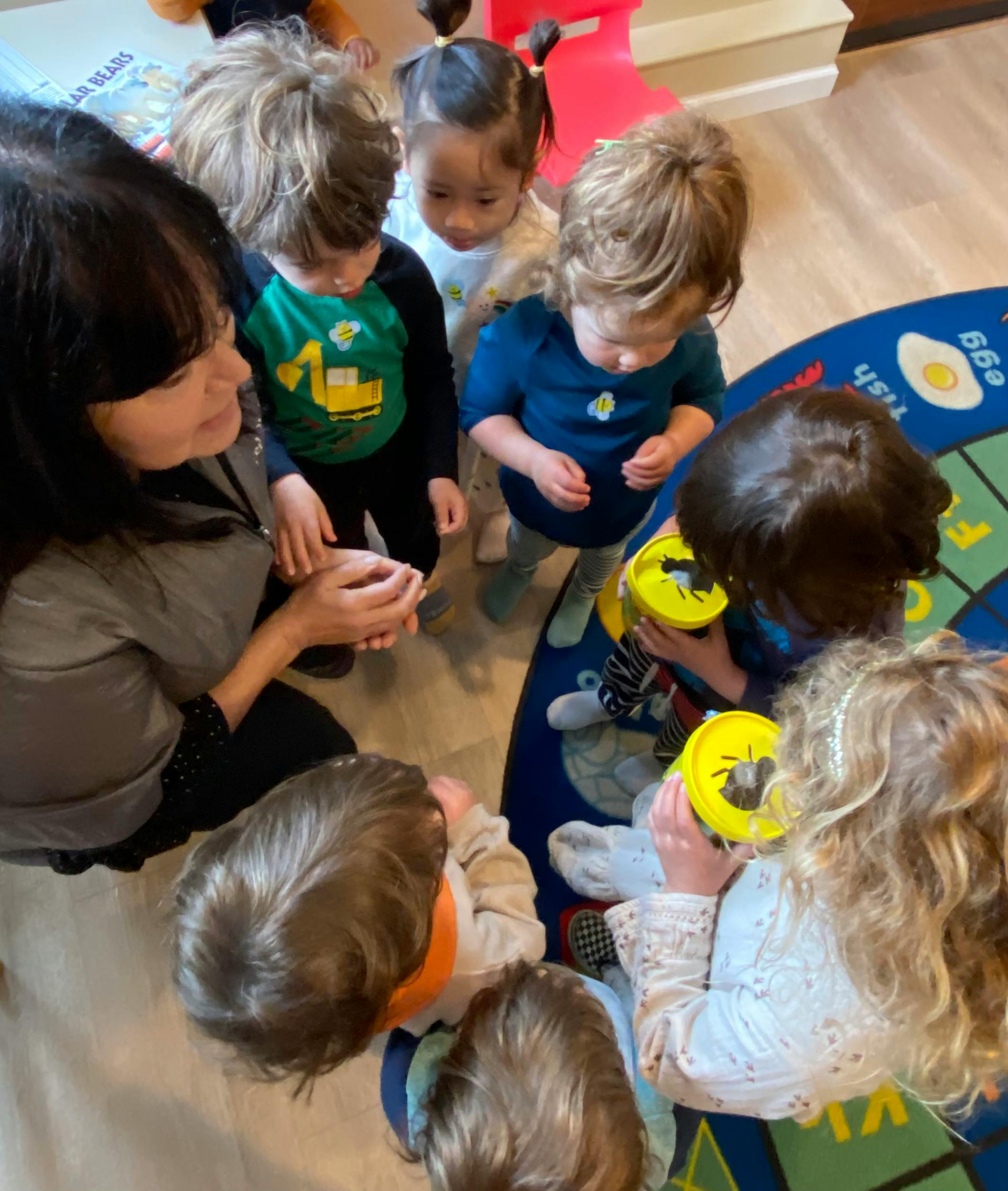 Adult and group of children interacting with small containers in a classroom