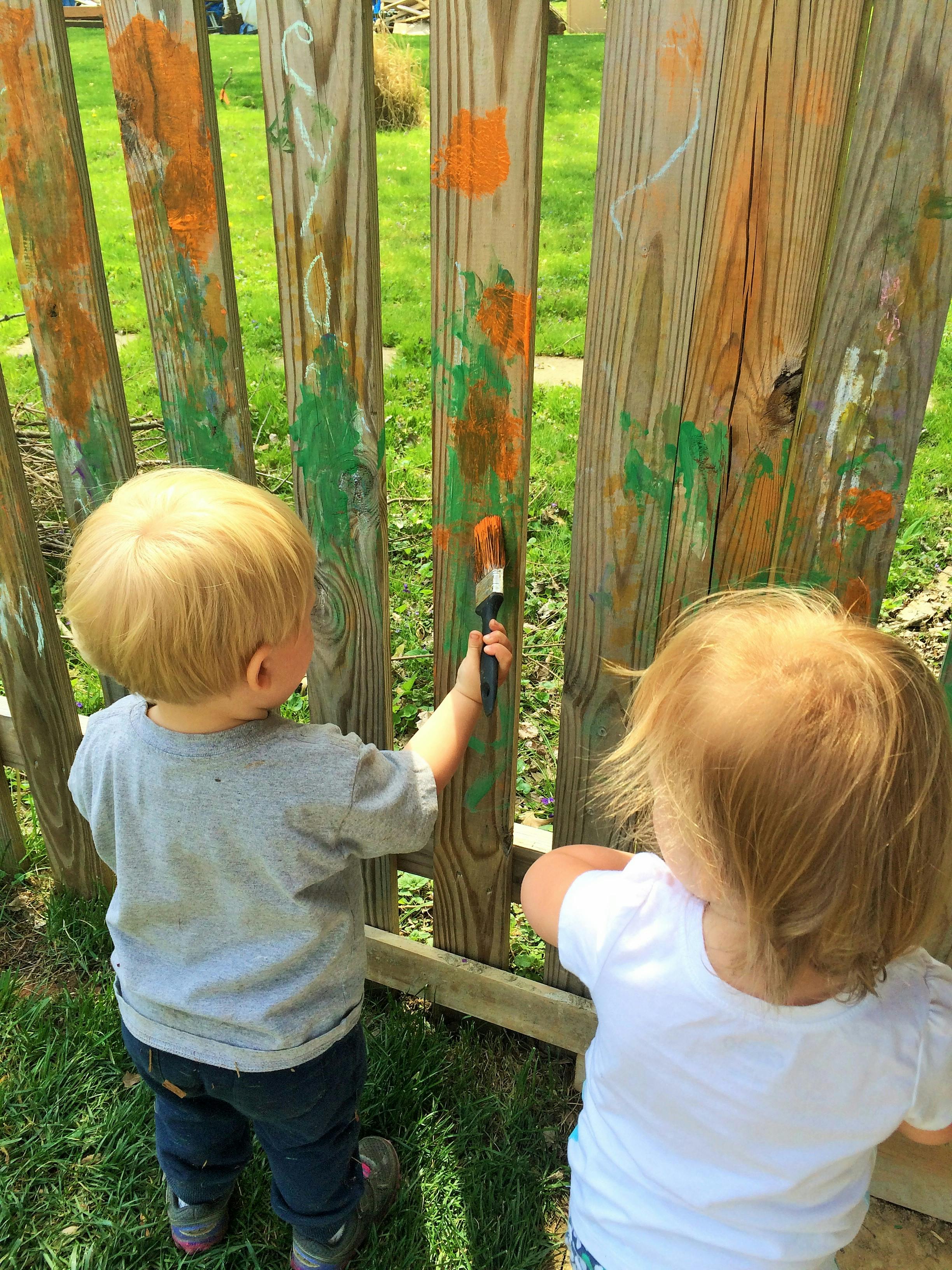 Two children painting a wooden fence
