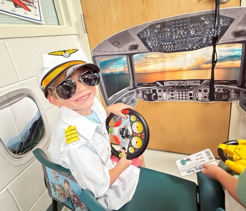 Child wearing a pilot costume holding a steering wheel in a simulated cockpit