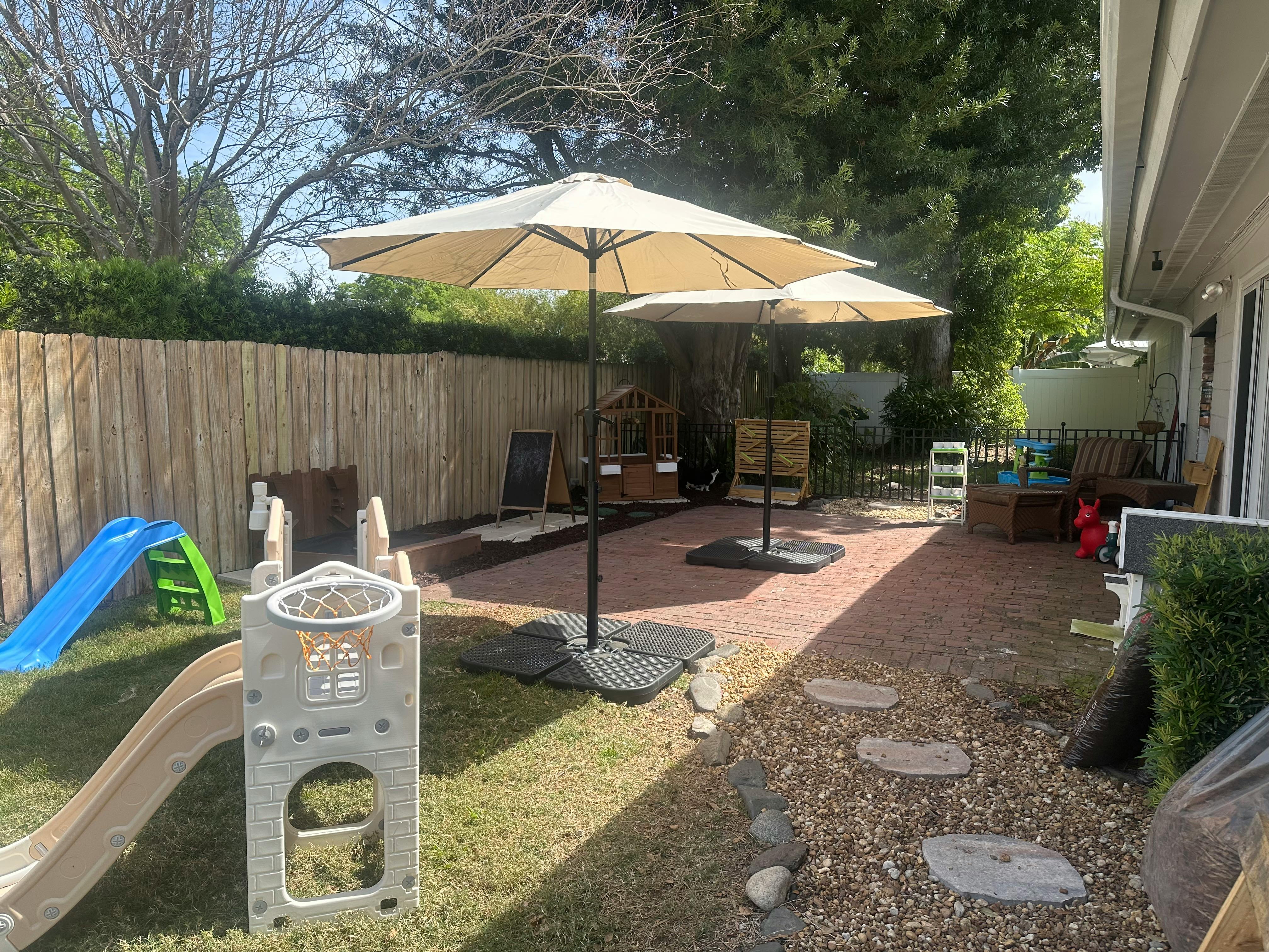 Backyard with patio umbrellas, play equipment, and a wooden fence