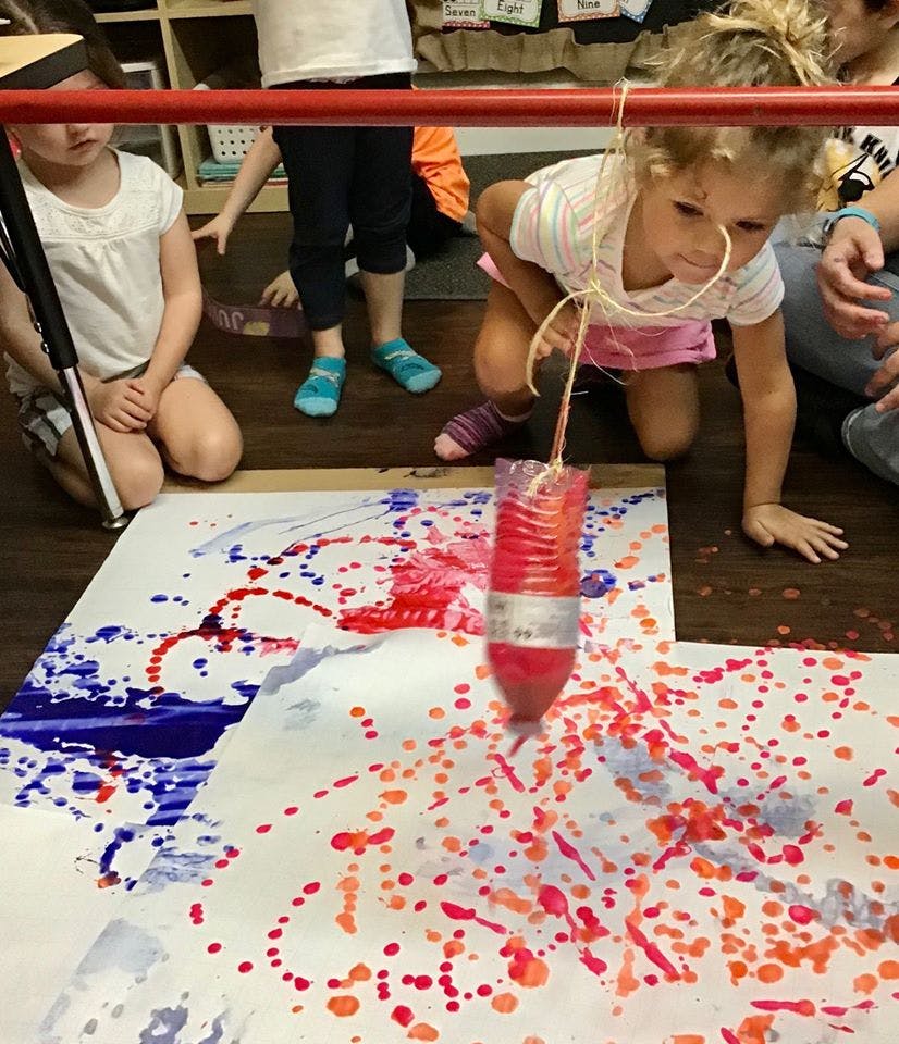 Child painting with a suspended bottle over paper