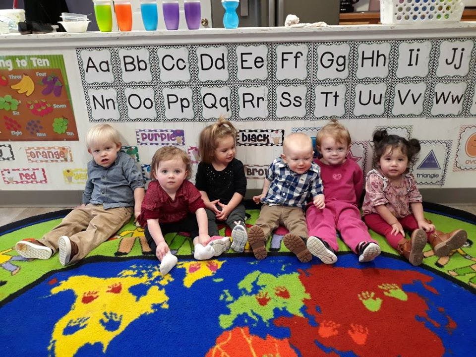 Six children sitting on a world map rug in front of an alphabet chart