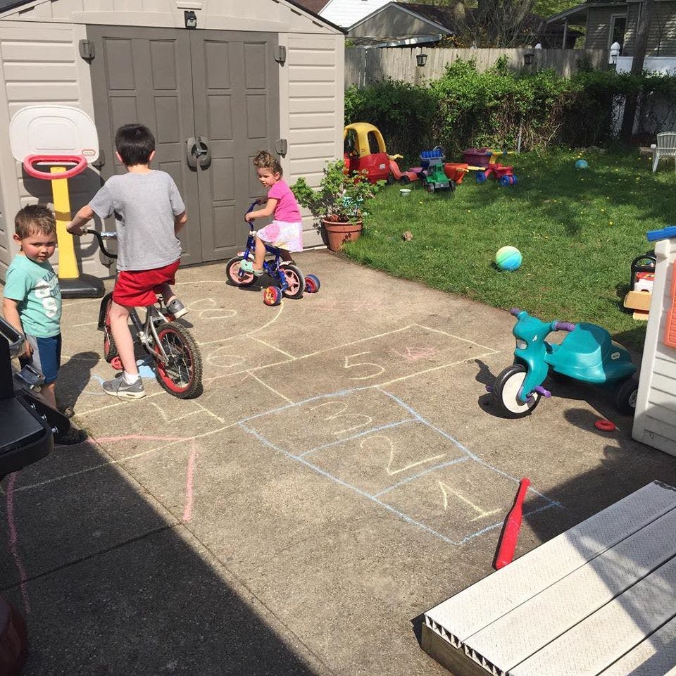 Three children playing with bikes and tricycles on a patio with chalk drawings