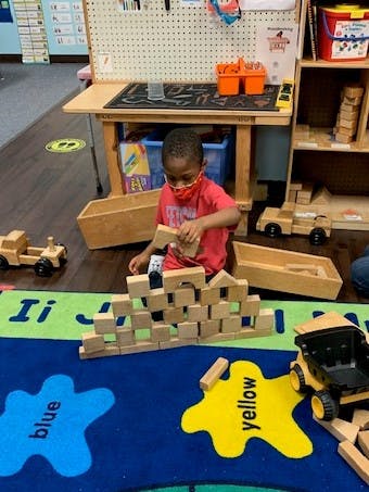 Child in a red shirt building with wooden blocks on a colorful rug