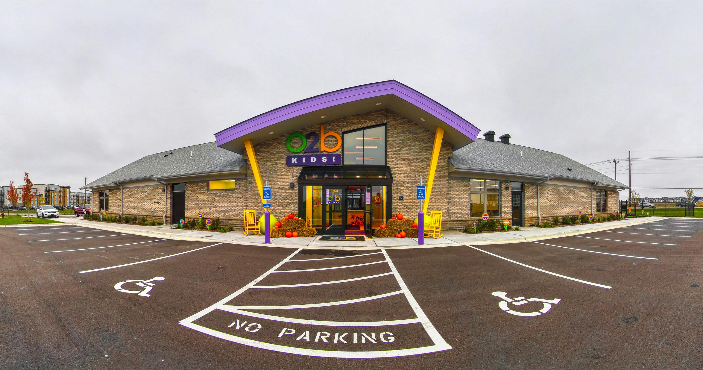 Brick building with a colorful O2B Kids! sign above the entrance and a parking lot
