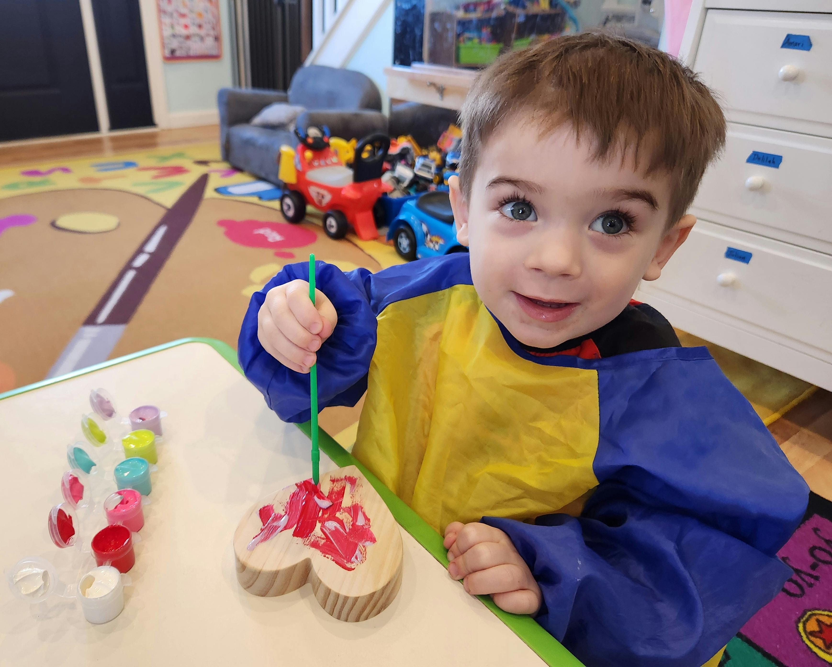 Child in a smock painting a wooden heart with red paint