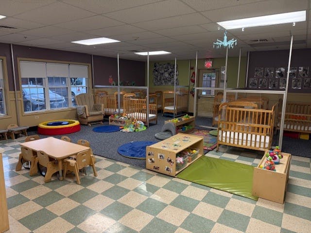 A childcare room with multiple cribs, a small table and chairs, and play mats