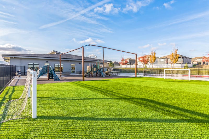 Playground with turf soccer field and building under a blue sky