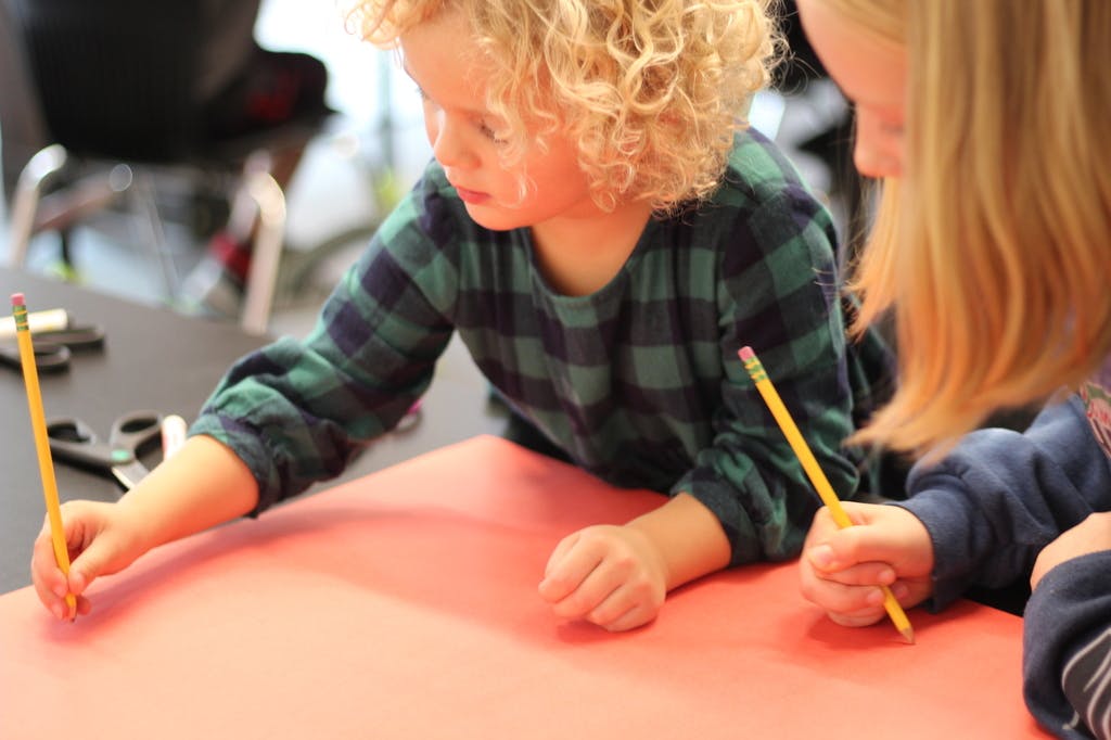 Two children drawing with pencils on red paper