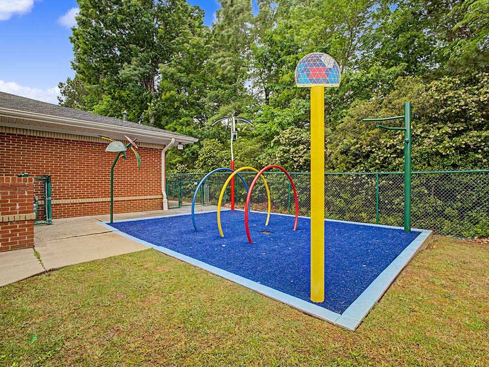 Colorful water playground with spray features on blue soft ground next to a brick building