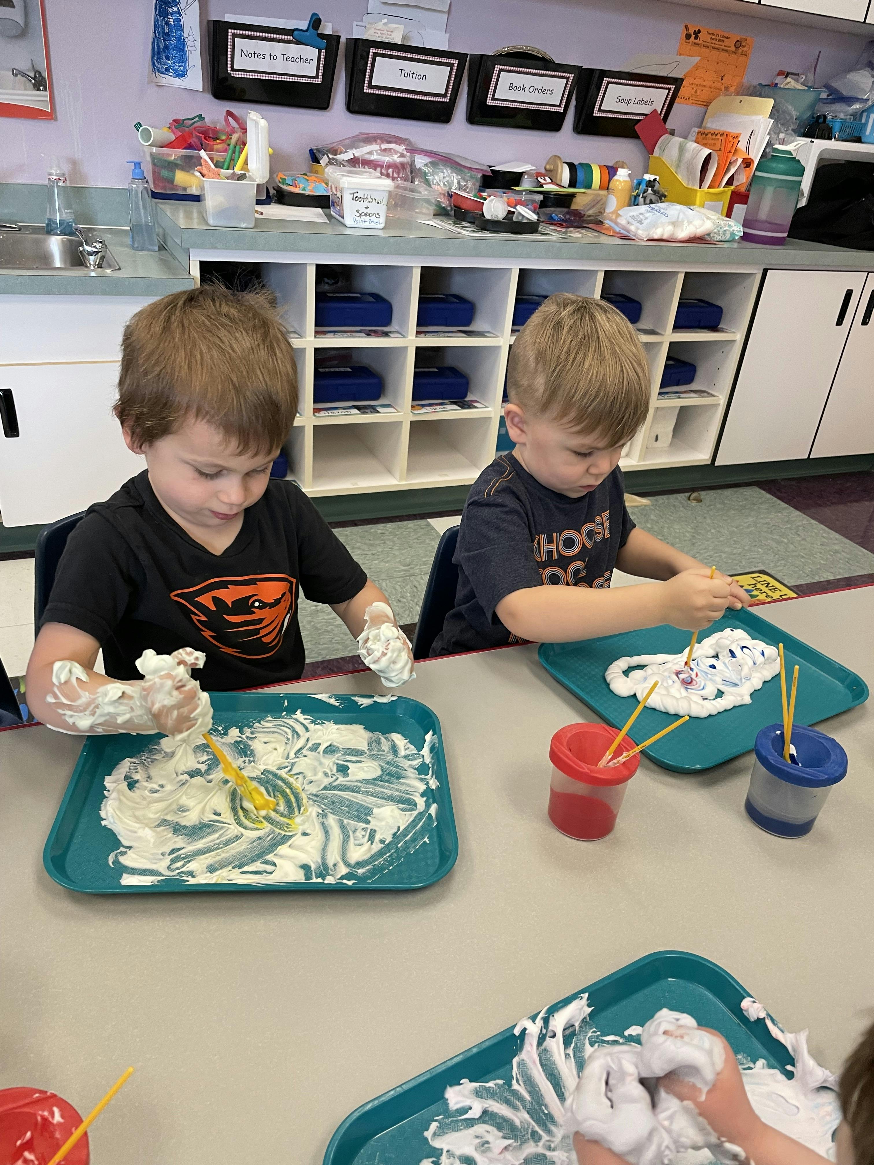 Two children at a table playing with shaving cream and paint