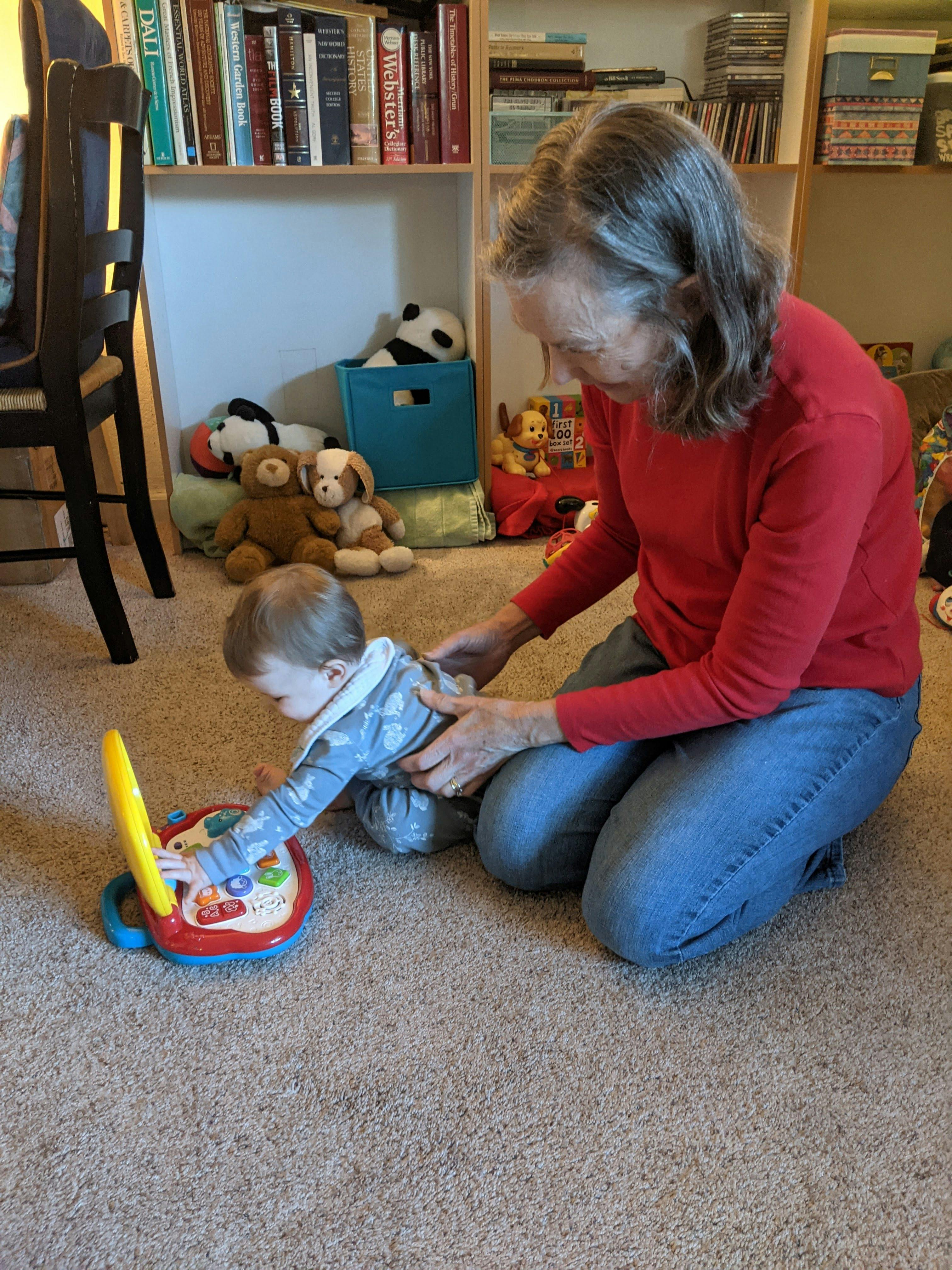 Person kneeling on carpet with child playing with toy