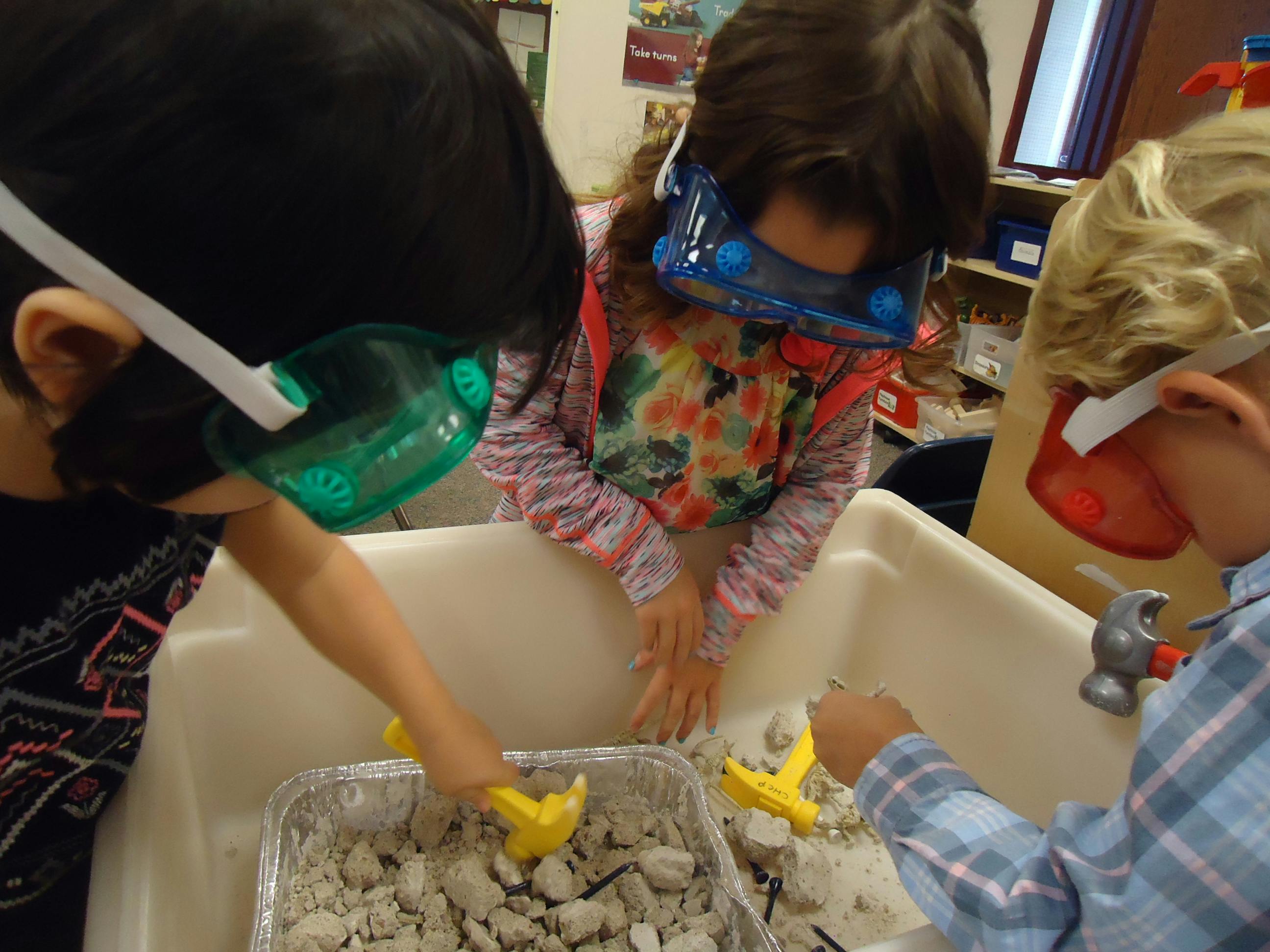 Three children wearing safety goggles playing in a classroom