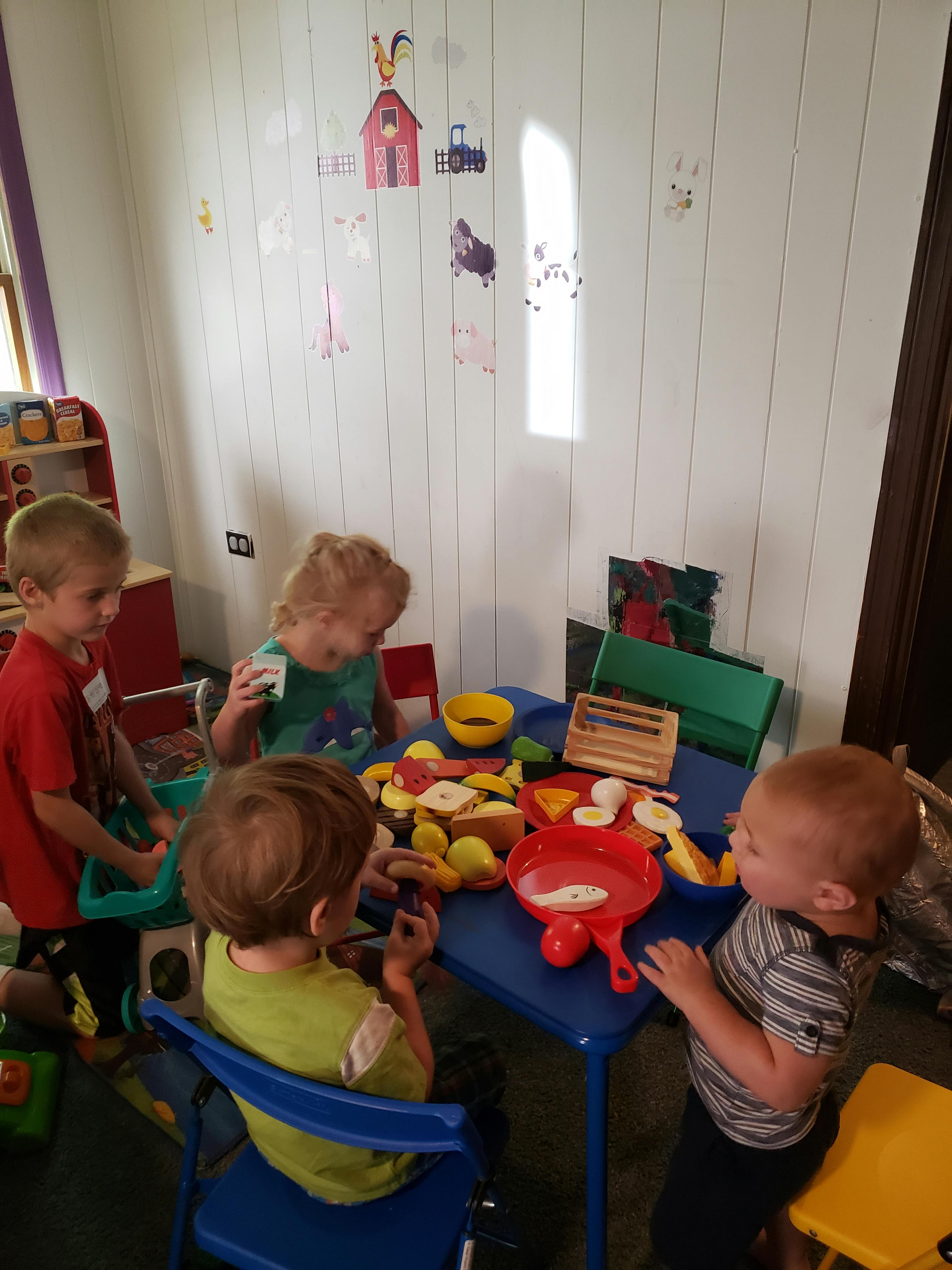 Four children playing with toy food at a small blue table