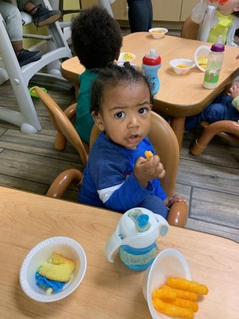 Child sitting at a table with snacks and holding a snack