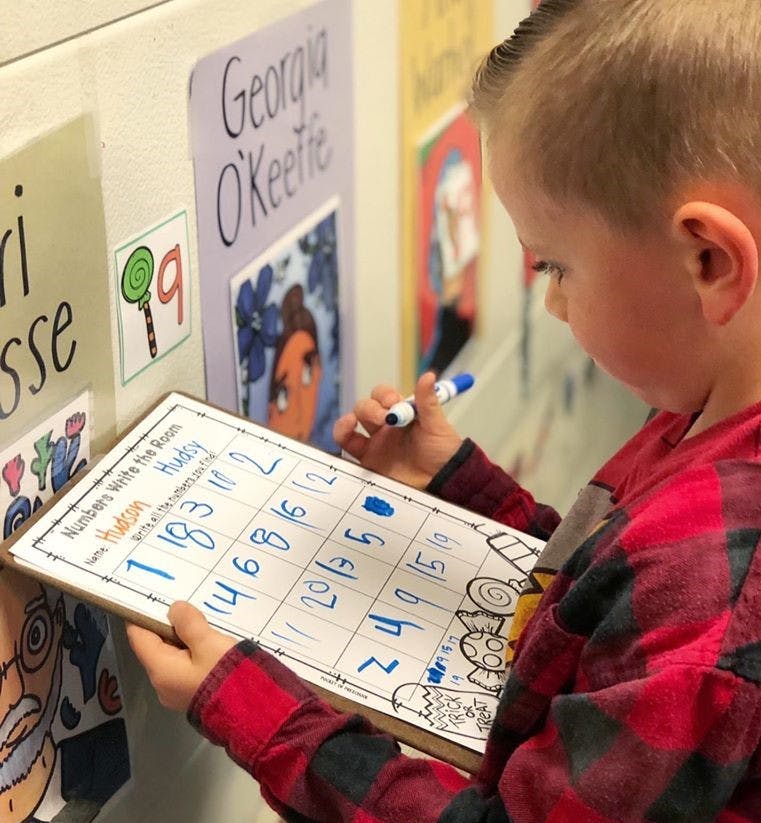 Child writing numbers on a whiteboard in a classroom