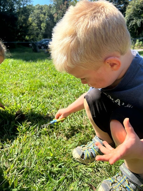 Child crouching in grass, holding a small tool