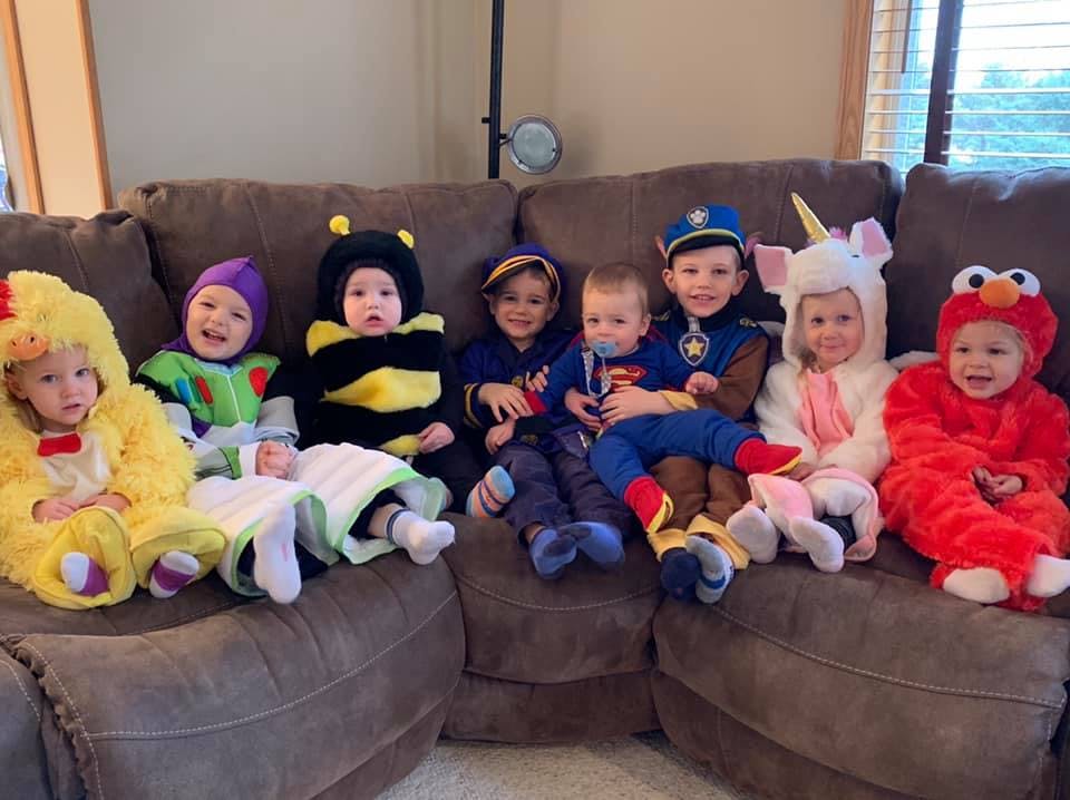 Seven children in various costumes sitting on a couch