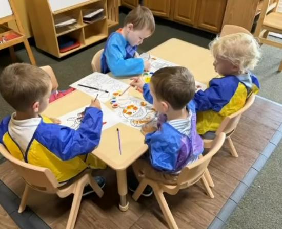 Four children painting on paper at a table in a classroom