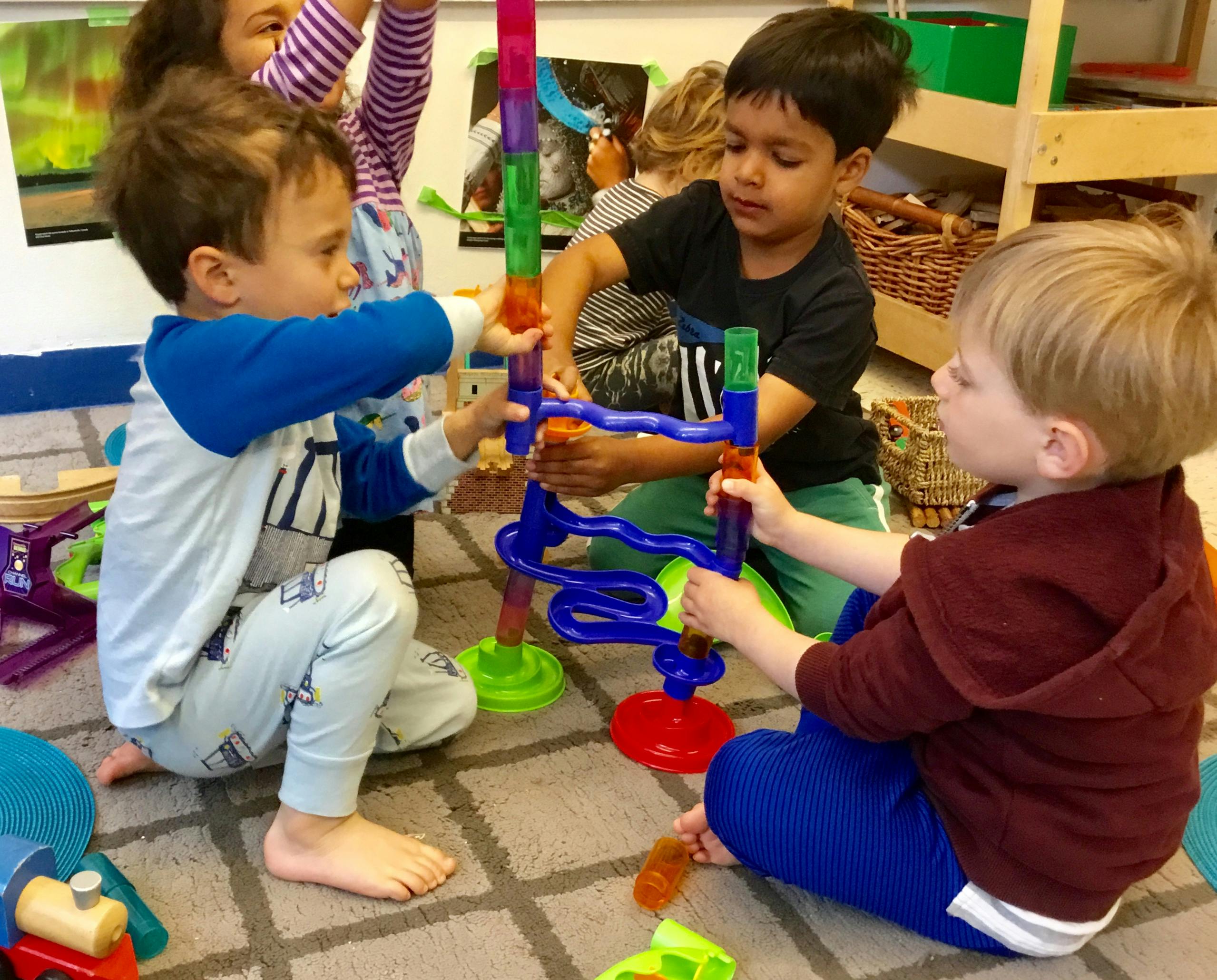Three children playing with a colorful marble run toy on the floor