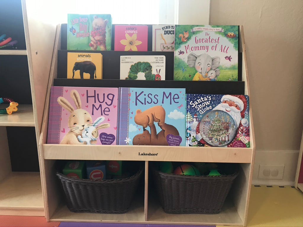 Children's books displayed on a wooden shelf with storage bins below