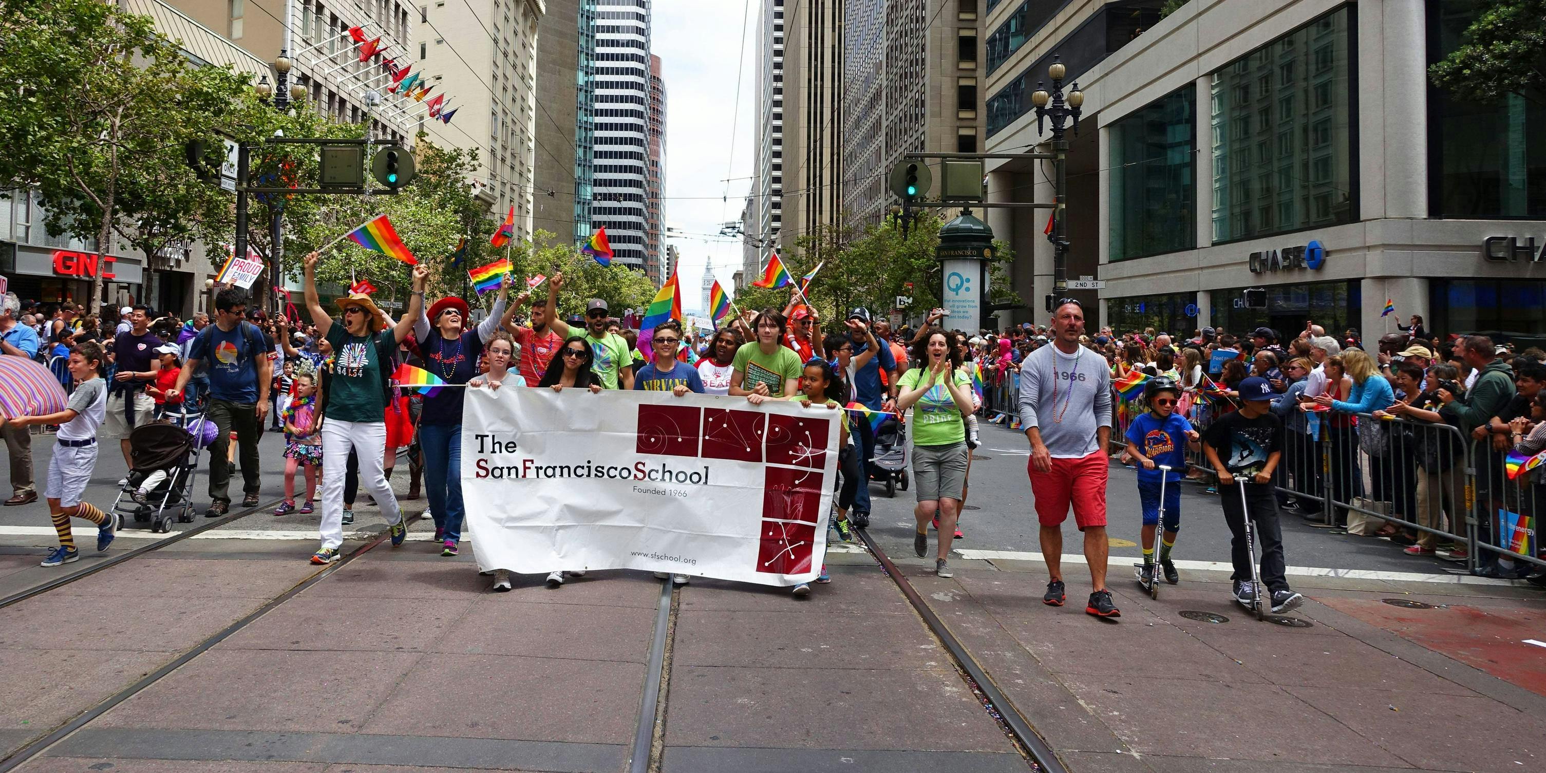 People marching in a parade with a banner and rainbow flags
