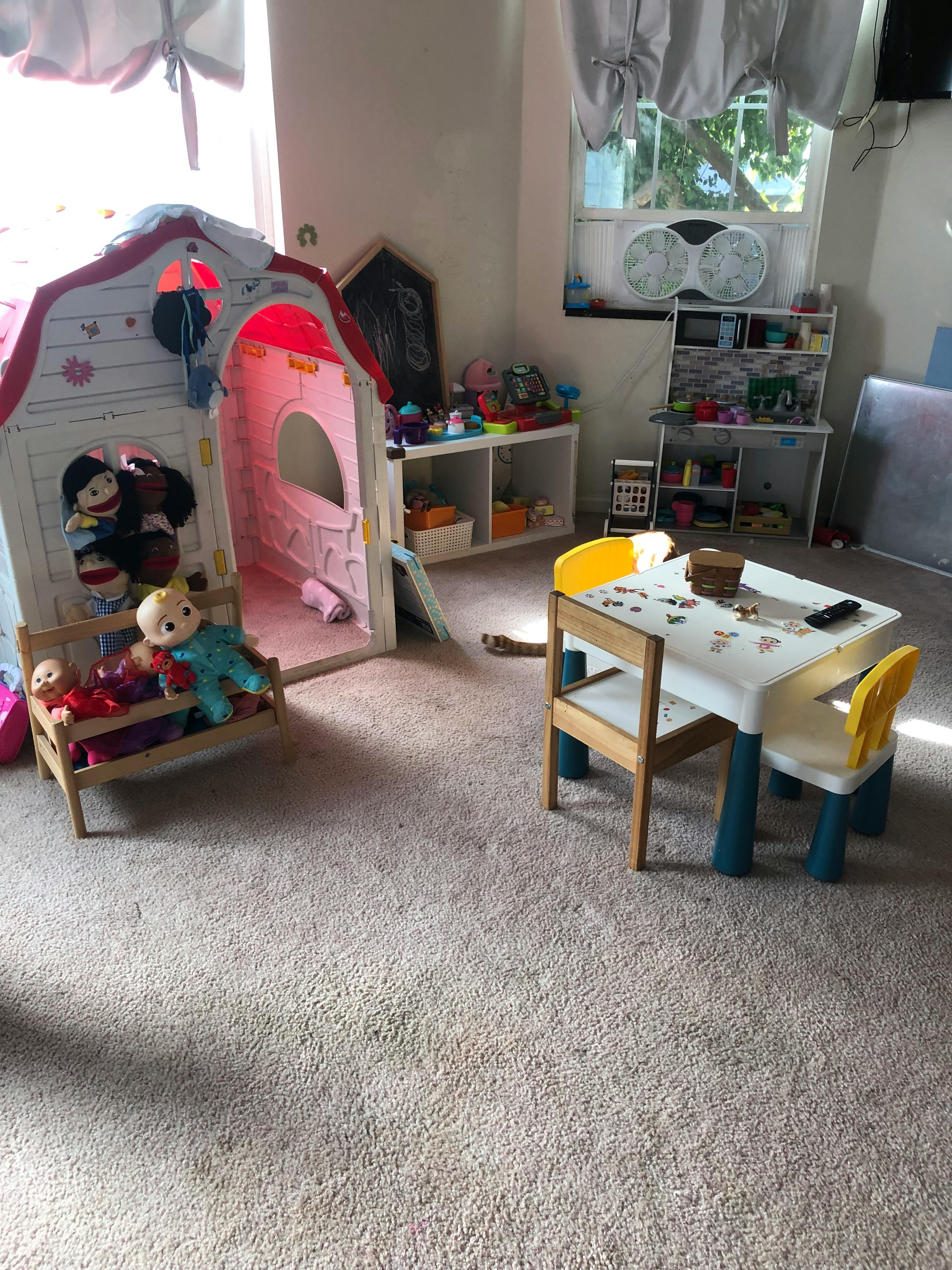 Playroom with a toy house, small table and chairs, and shelves with dolls