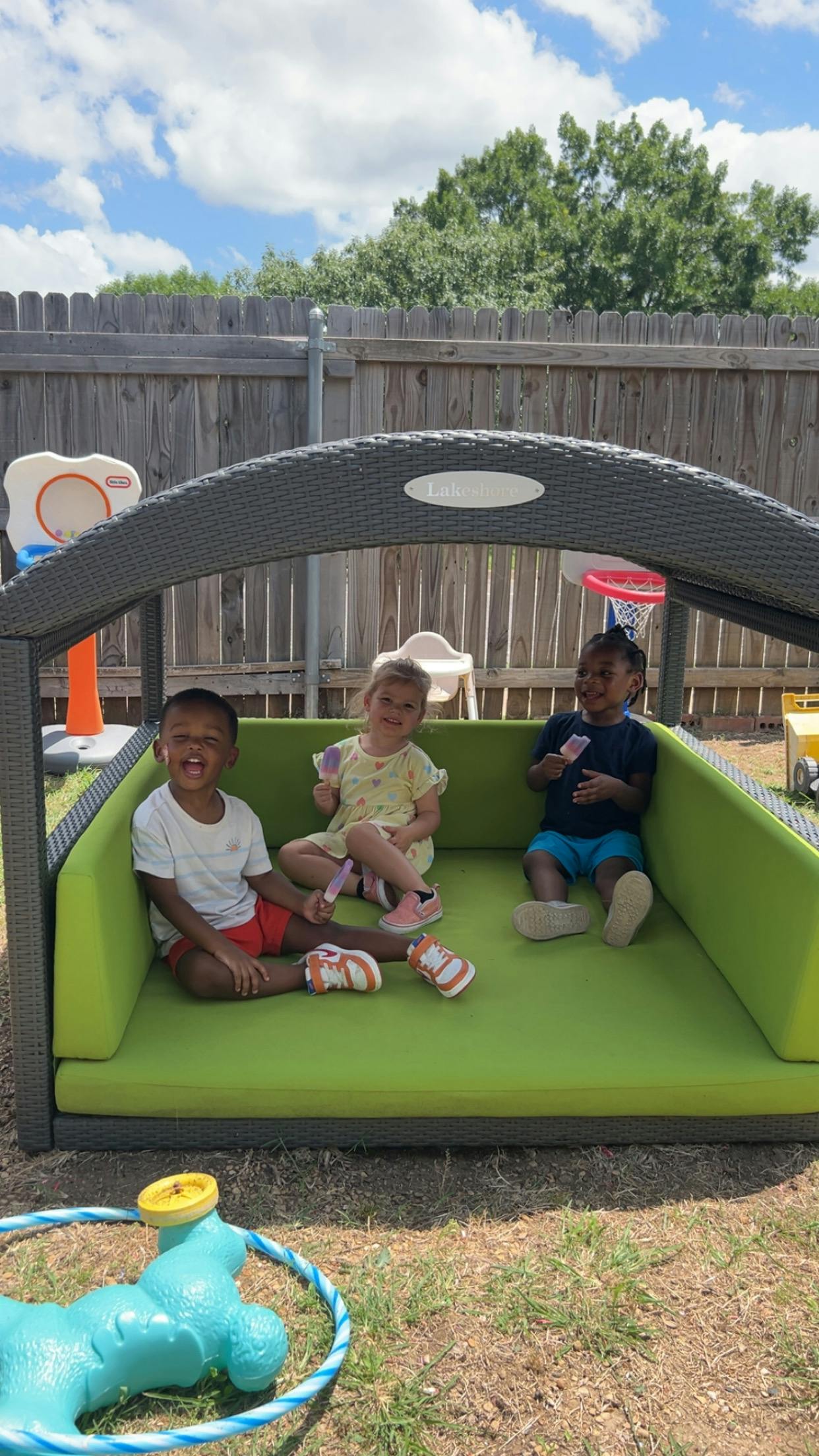 Three children sitting on a green cushion under a canopy