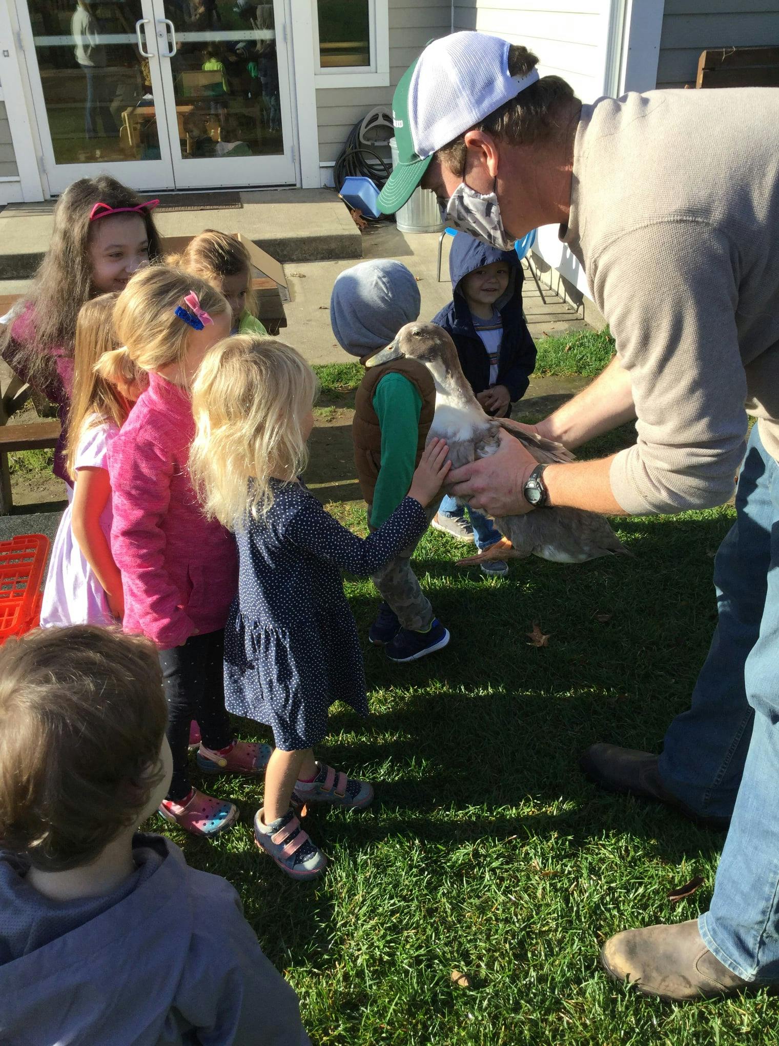 Adult holding a goat while children gather around to pet it