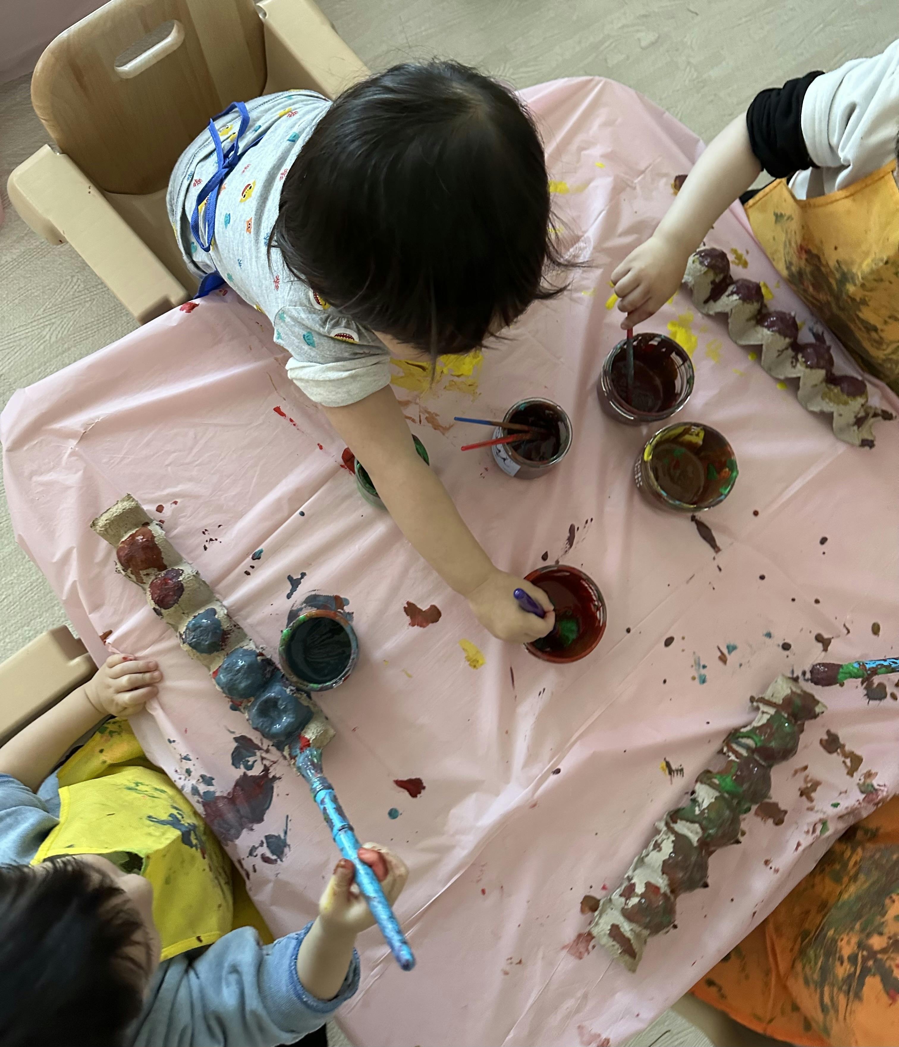 Children painting egg cartons with brushes at a table