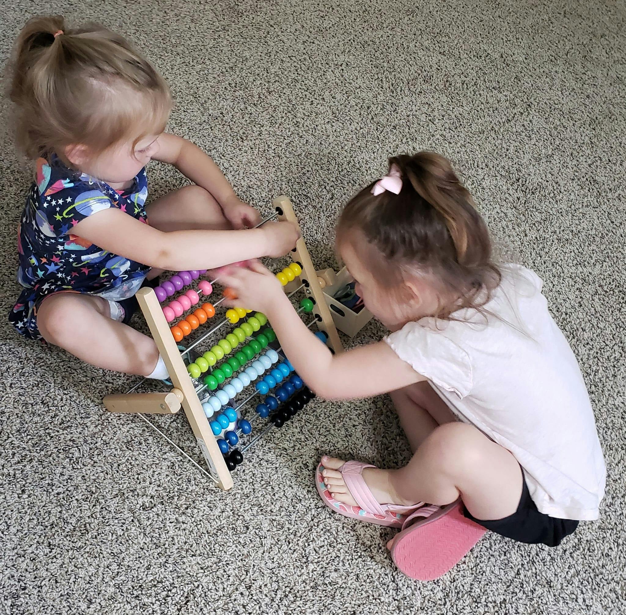 Two children playing with a colorful abacus on the floor